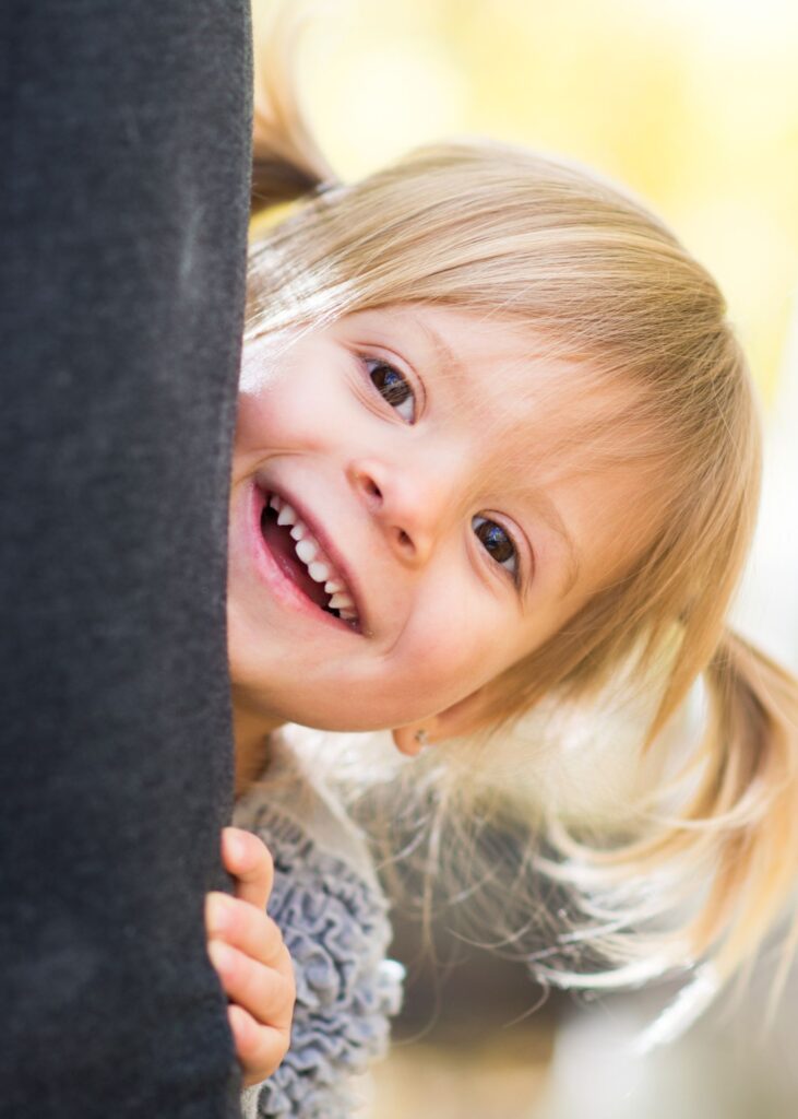 Curious 6 year old blonde girl peeking from behind a tree